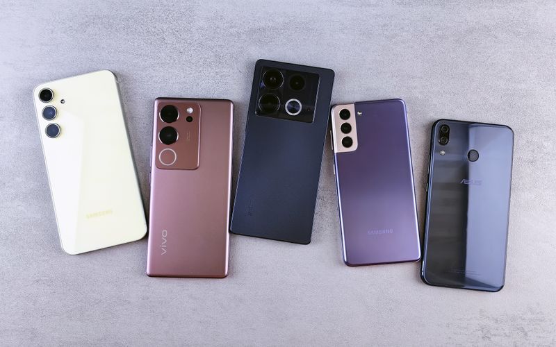 Flat lay of five modern smartphones on a gray surface, showcasing various designs and brands