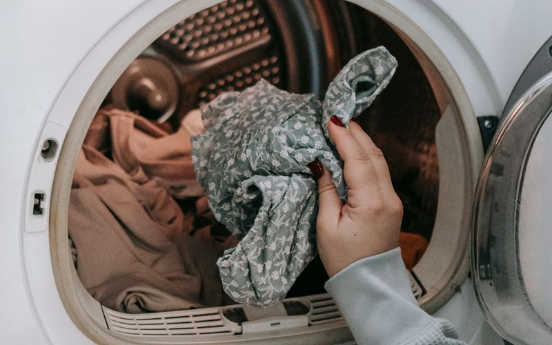 Woman loading dirty clothes into a modern white washing machine in a light room at home